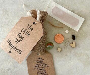 En liten tygpåse med texten 'The Little Bag of Happiness' och tillhörande småsaker.