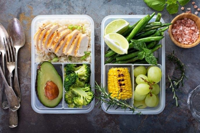 Två matlådor med kyckling, ris, grönsaker, frukt och lime