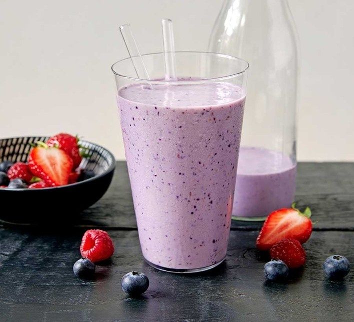 Lila bärsmoothie i glas med färska jordgubbar och blåbär