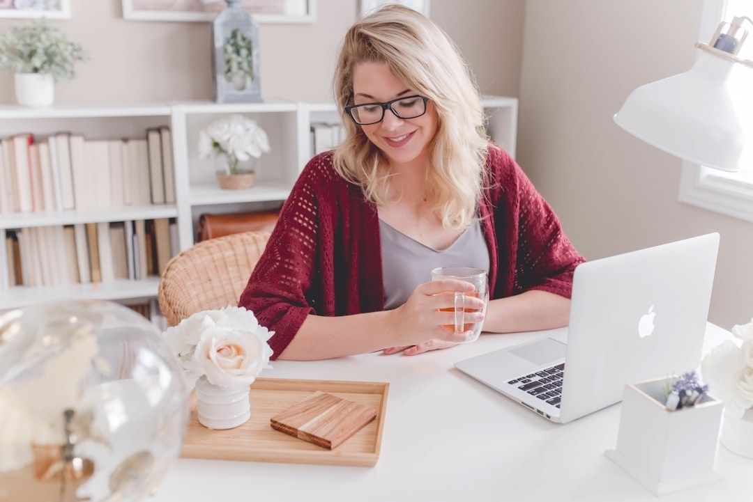 Kvinna med glas och laptop arbetar vid ett ljust skrivbord